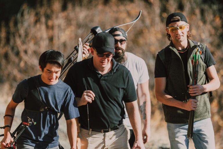 Four men practicing archery outdoors, equipped with bows and arrows.